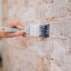 ręka z pędzlem malująca ścianę ceglaną