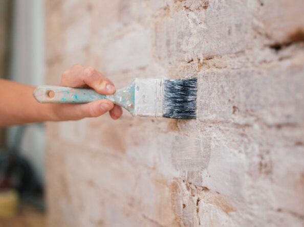 ręka z pędzlem malująca ścianę ceglaną